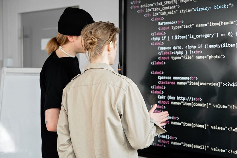 Zwei professionelle Webentwickler der Internetagentur 5150media prüfen und programmieren sauberen HTML5-Quellcode auf einem großen Monitor zur Optimierung einer Kundenwebseite