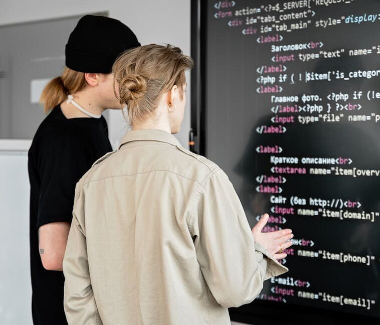 Zwei professionelle Webentwickler der Internetagentur 5150media prüfen und programmieren sauberen HTML5-Quellcode auf einem großen Monitor zur Optimierung einer Kundenwebseite